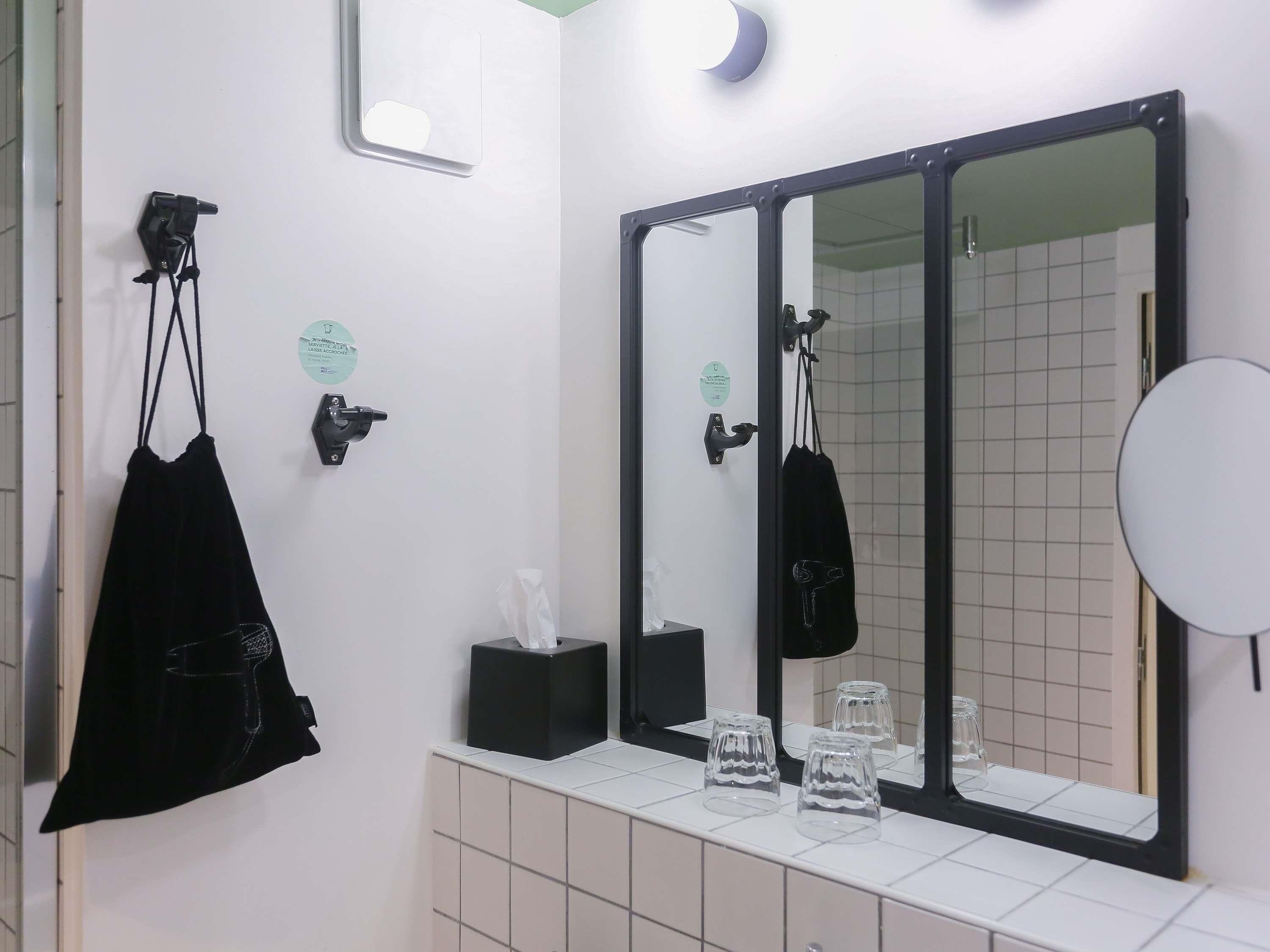 A bathroom with a large mirror, a towel rack, a tissue box, and a glass set on the counter.