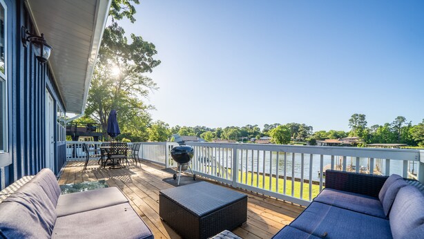 Eine Terrasse mit Gartenmöbeln, einem Grill und Blick auf ein Gewässer.