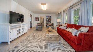 Ein geräumiges Wohnzimmer mit einem roten Sofa, einer weißen Unterhaltungseinheit und einem gemusterten Teppich.