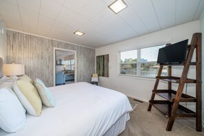 A bedroom with a large bed, a TV on a wooden stand, and a window with blinds.