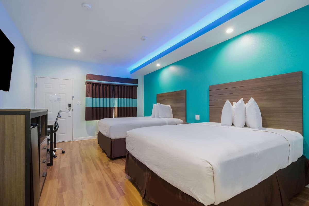 A hotel room with two beds, a desk, and a door.