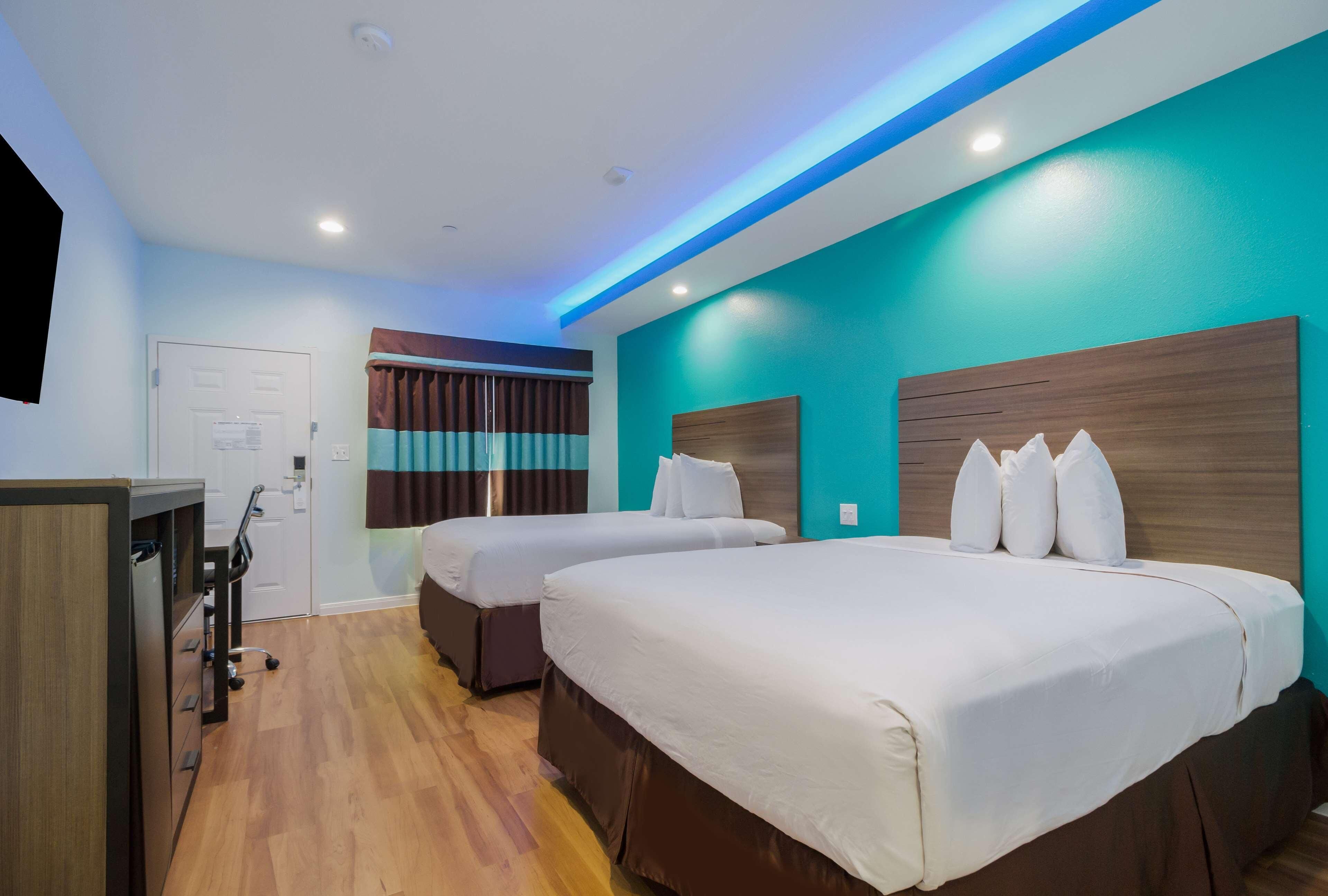 A hotel room with two beds, a desk, and a door.