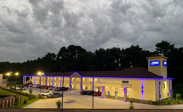 A motel with a parking lot, a building with a blue-lit exterior, and a sign indicating it is part of the Americas hotel chain. - Americas Best Value Inn Aldine Westfield (Humble)