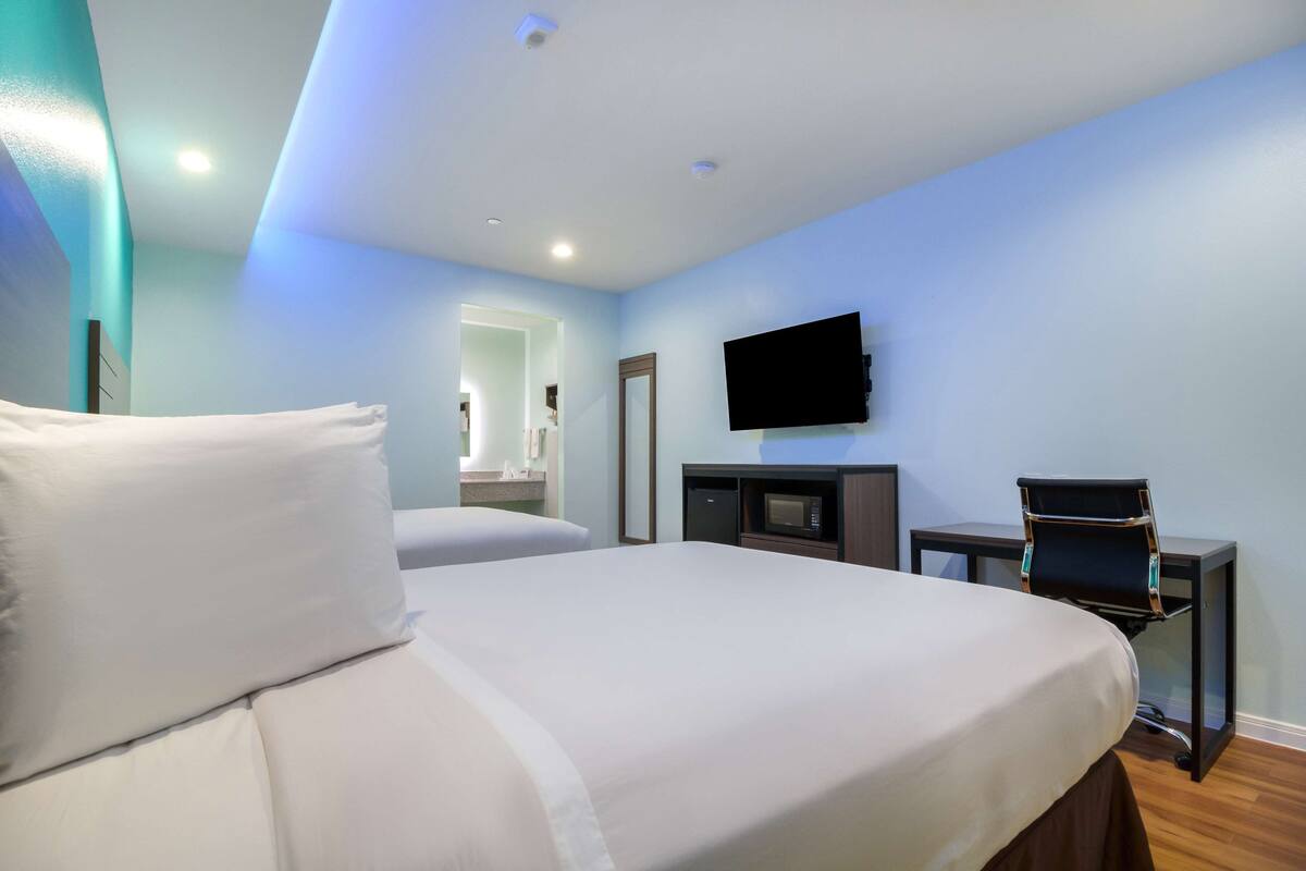 A hotel room with a bed, a TV mounted on the wall, a desk with a chair, and a microwave.