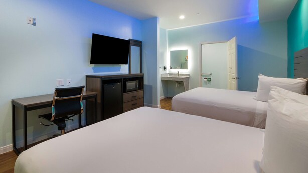 Una habitación de hotel con cama, escritorio, silla, televisor y baño con espejo y lavamanos.