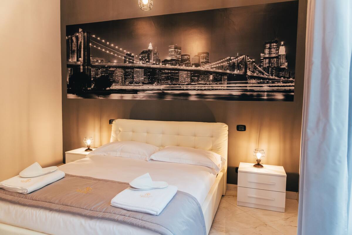 Une chambre d’hôtel avec un grand lit, deux tables de chevet et un tableau représentant un paysage urbain accroché au-dessus du lit.