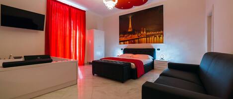 A modern bedroom with a bed, a black leather sofa, a red curtain, a white cabinet, a flat-screen TV, and a cityscape painting on the wall.
