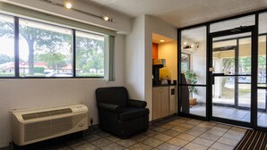 A room with a large window, an air conditioning unit, a black chair, a kitchen area with cabinets, and a door leading outside. - Days Inn by Wyndham Charlotte University (Charlotte)