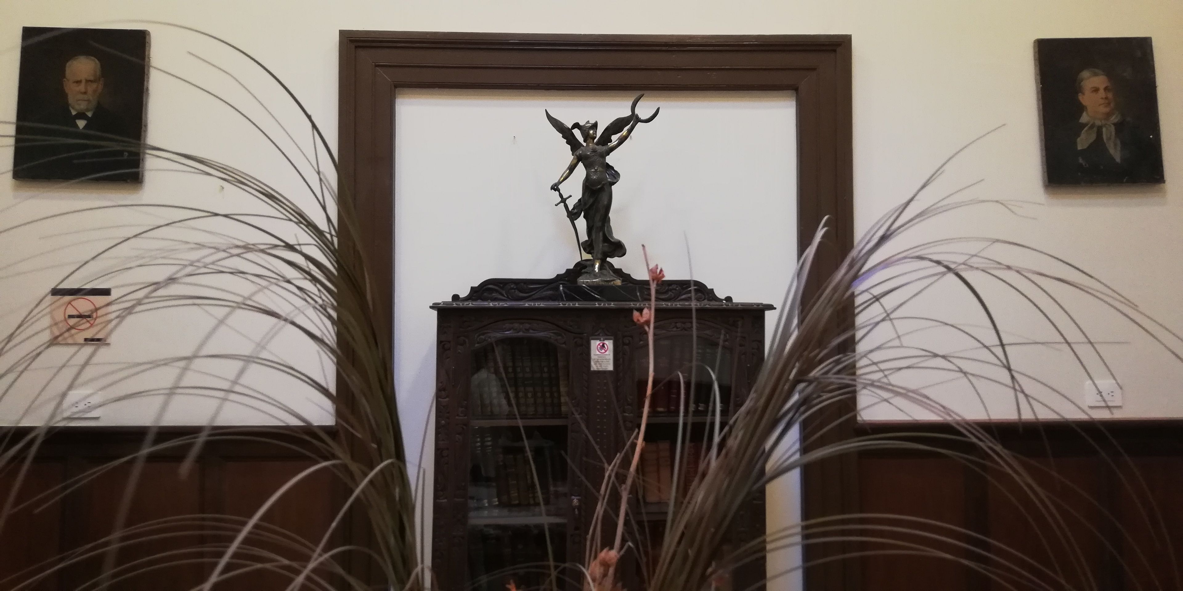 Una estatua sobre un pedestal en una habitación con dos retratos enmarcados en las paredes.