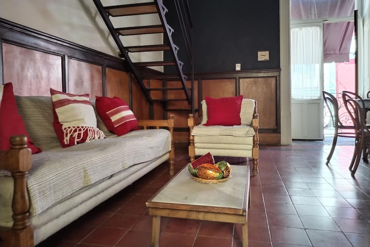 Uma sala de estar com um sofá, duas poltronas, uma mesa de centro e uma escada.