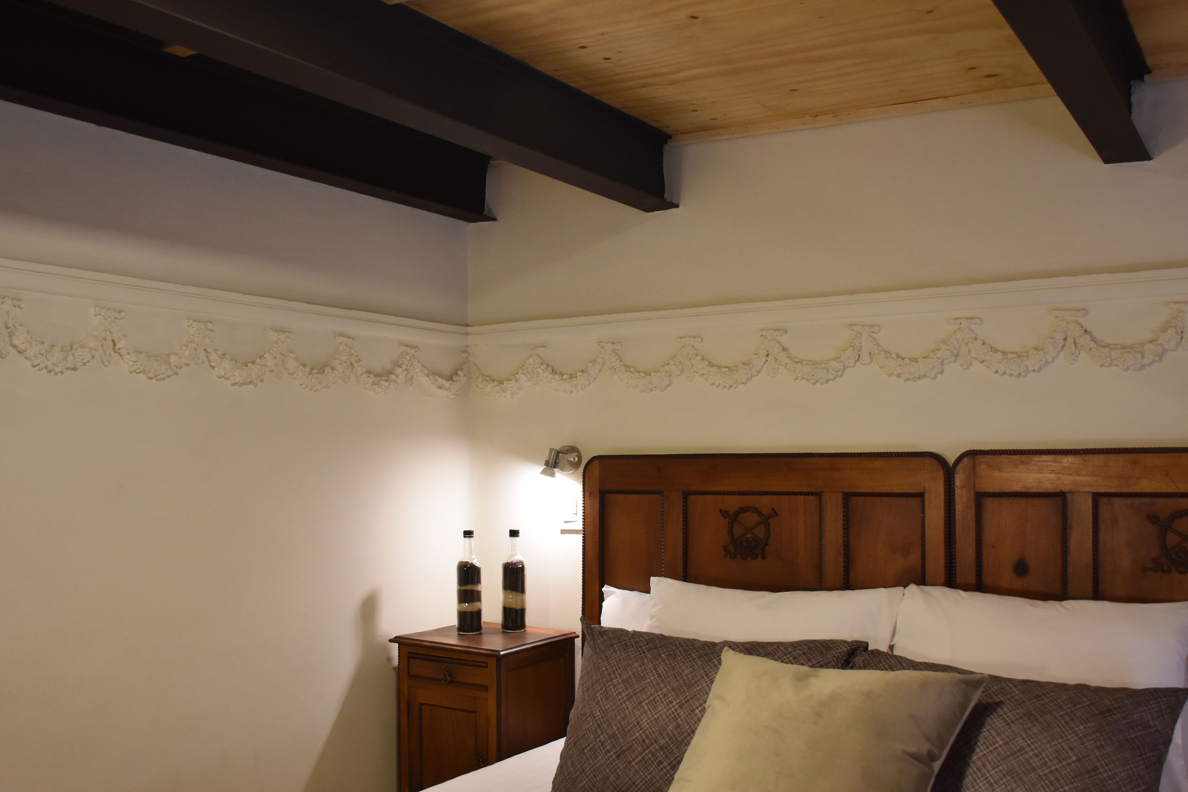 Un dormitorio con cabecera de madera, una mesita de noche con botellas y un zócalo decorativo.