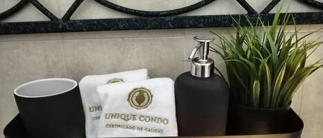 A black tray with a black tumbler, a black bottle, a white towel with a gold emblem, and a green plant.