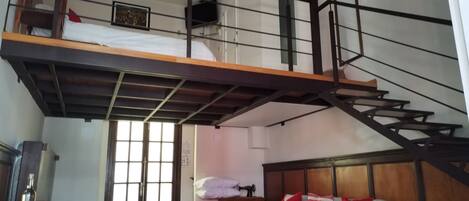 Une chambre de style « loft », avec un escalier en bois, un lit, un bureau et une chaise.