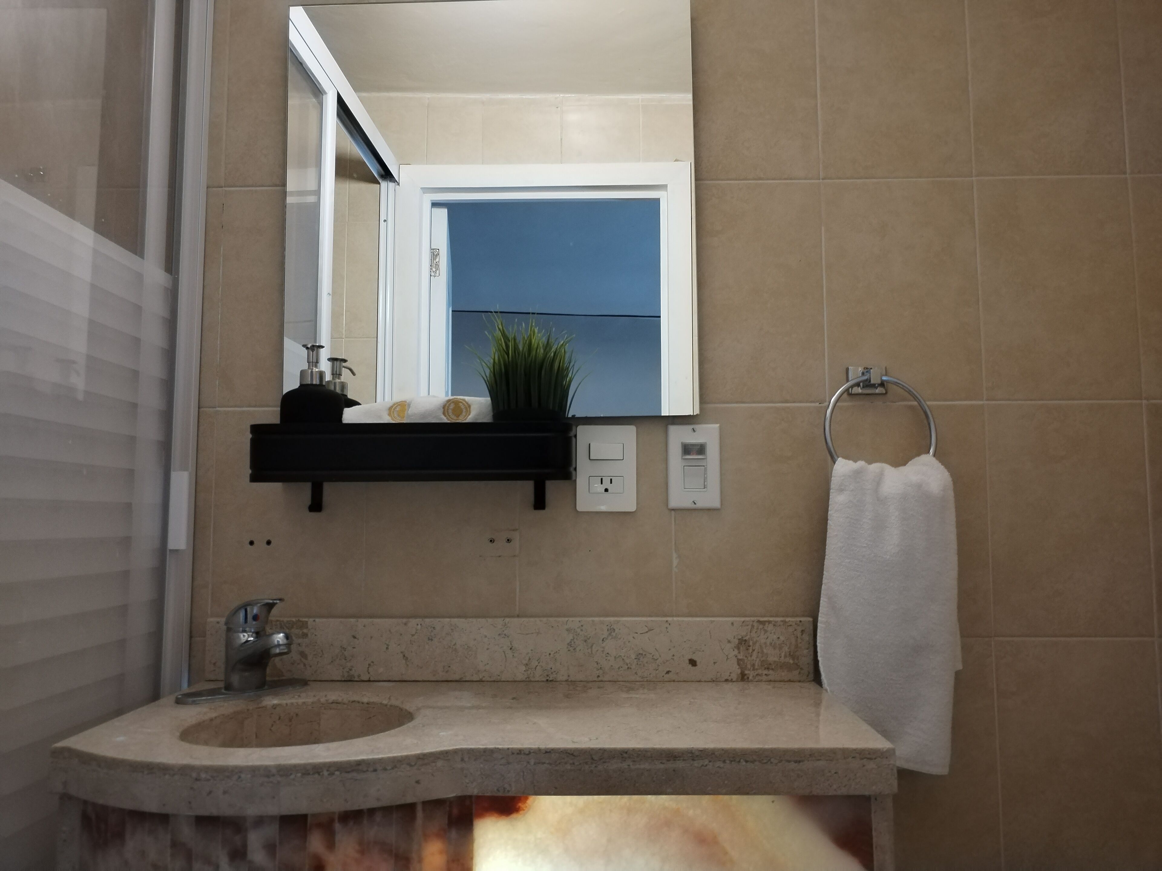 Une salle de bain équipée d’un lavabo, d’un miroir, d’un porte-serviettes et d’une étagère où sont rangés les articles de toilette.