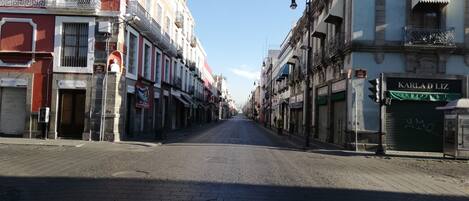Rua com edifícios, alguns com persianas fechadas, e céu claro acima.