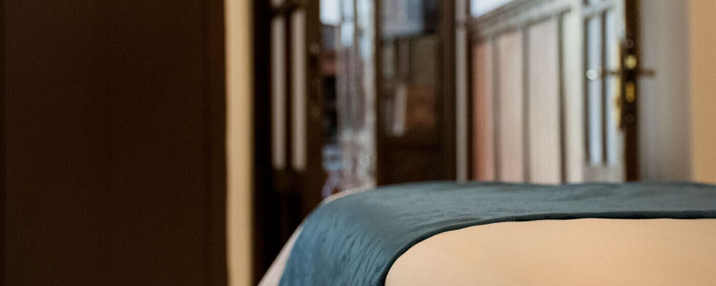 A hotel room with a bed, a door, and a view of the street outside.