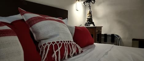 Ein ordentlich bezogenes Bett mit roter und weißer Bettwäsche, eine Wandleuchte und ein kleiner Tisch mit einem dekorativen Gegenstand.