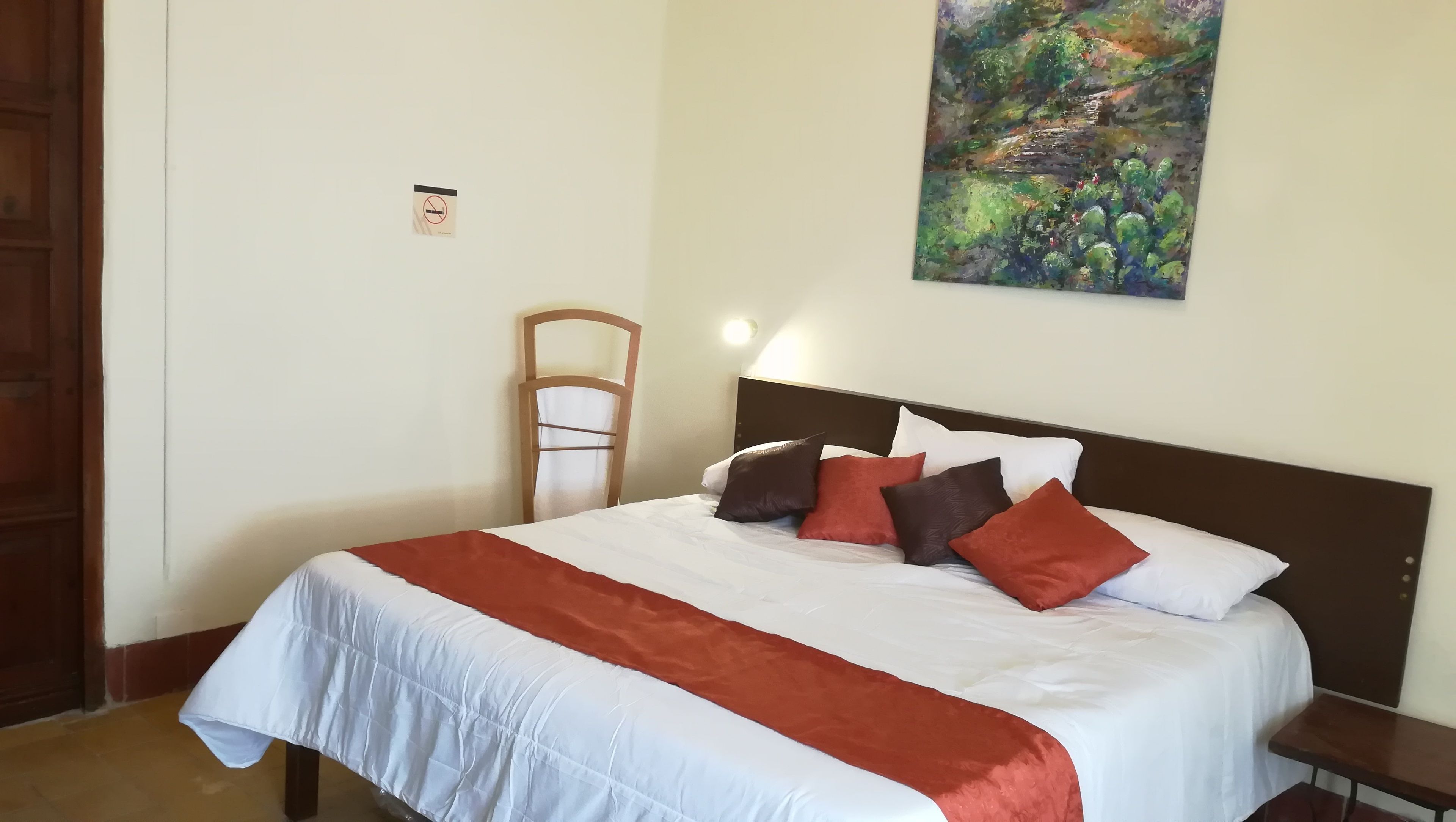 A neatly made bed with a white and red bedspread, a wooden headboard, and several pillows in red, brown, and white.