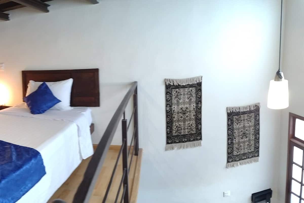 Quarto de hotel com duas camas, cabeceiras de madeira, piso de madeira, mesa de cabeceira com abajur e janela com vista para a cidade.