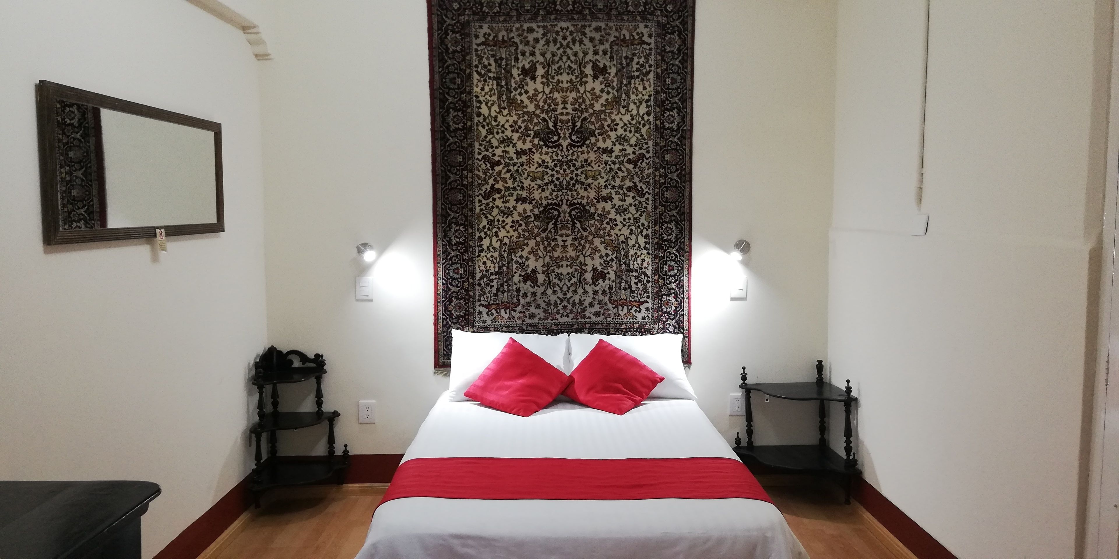 A hotel room with a bed, a nightstand, a mirror, and a decorative tapestry.