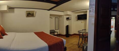 A hotel room with a bed, a desk, a chair, a TV, and a door leading to another room.