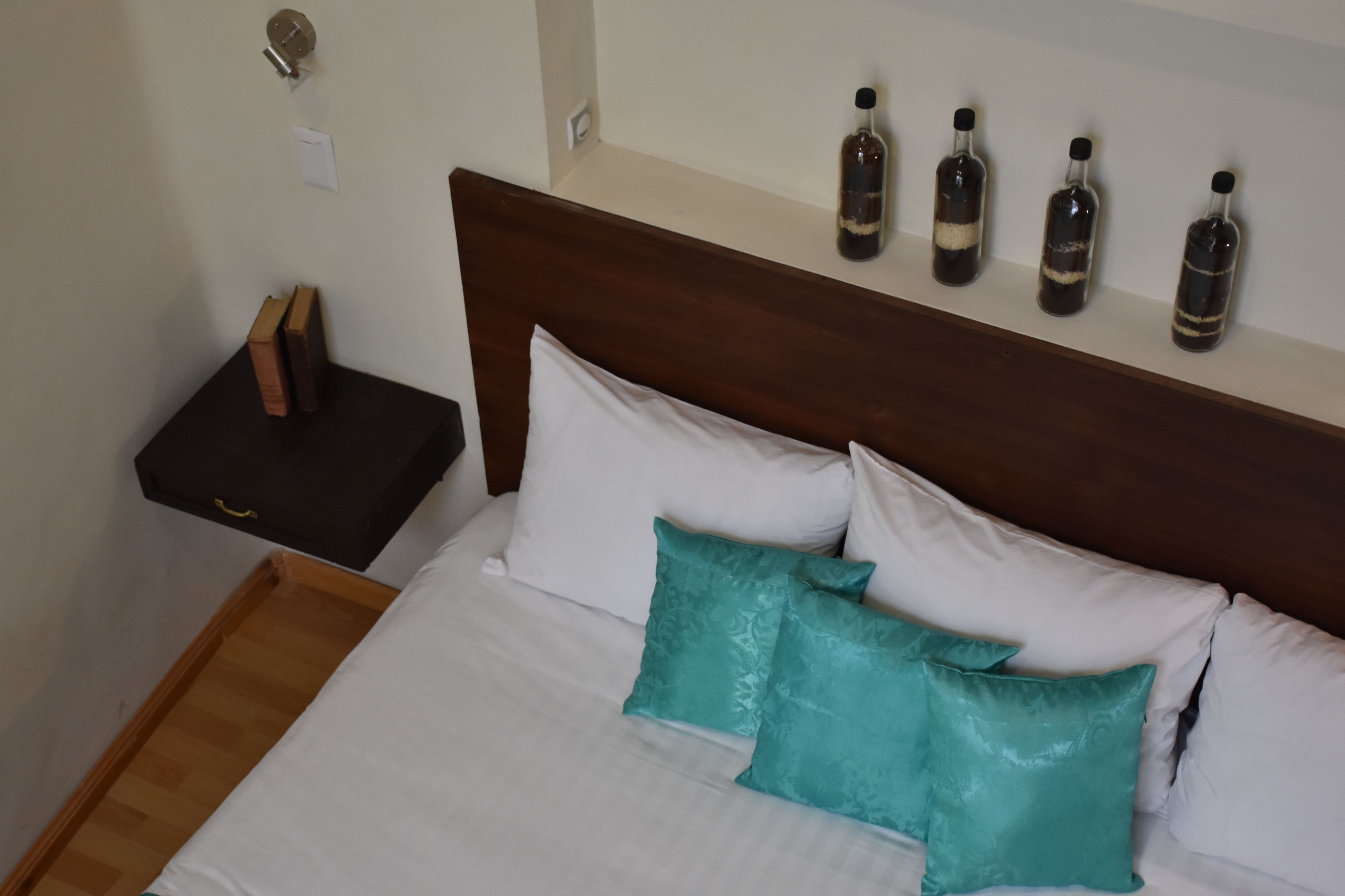 A neatly made bed with white and teal pillows, a wooden headboard, and a nightstand with books and a lamp.