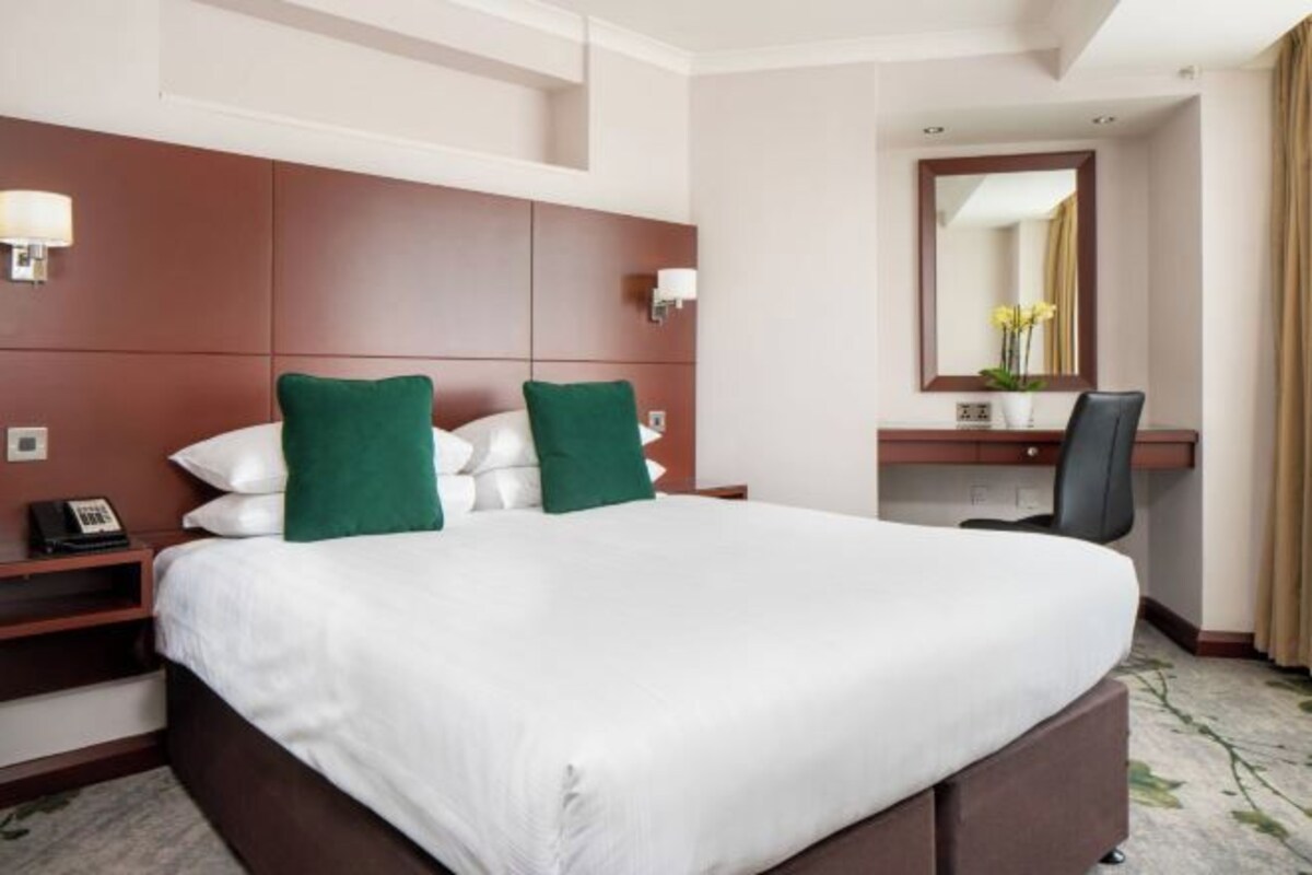 A hotel room with a large bed, a desk with a chair, a mirror, and a telephone on the nightstand.