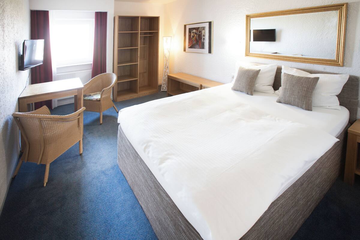 Ein Hotelzimmer mit einem großen Bett, einem Schreibtisch mit Stuhl, einem Kleiderschrank und einem Fernseher an der Wand.