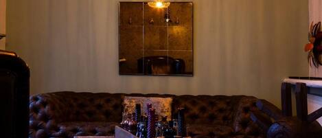 A cozy room with a tufted leather sofa, a wooden coffee table with bottles, and a large mirror on the wall.