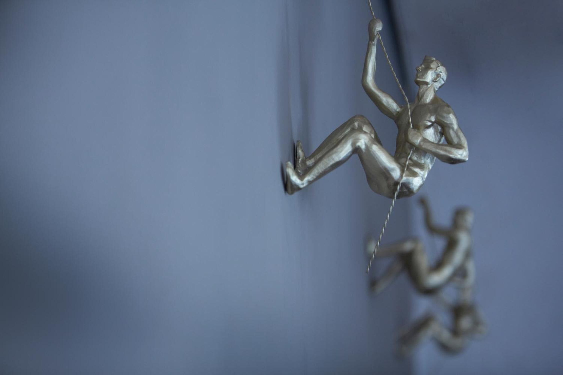 Une sculpture métallique représentant une personne en train d’escalader un mur.