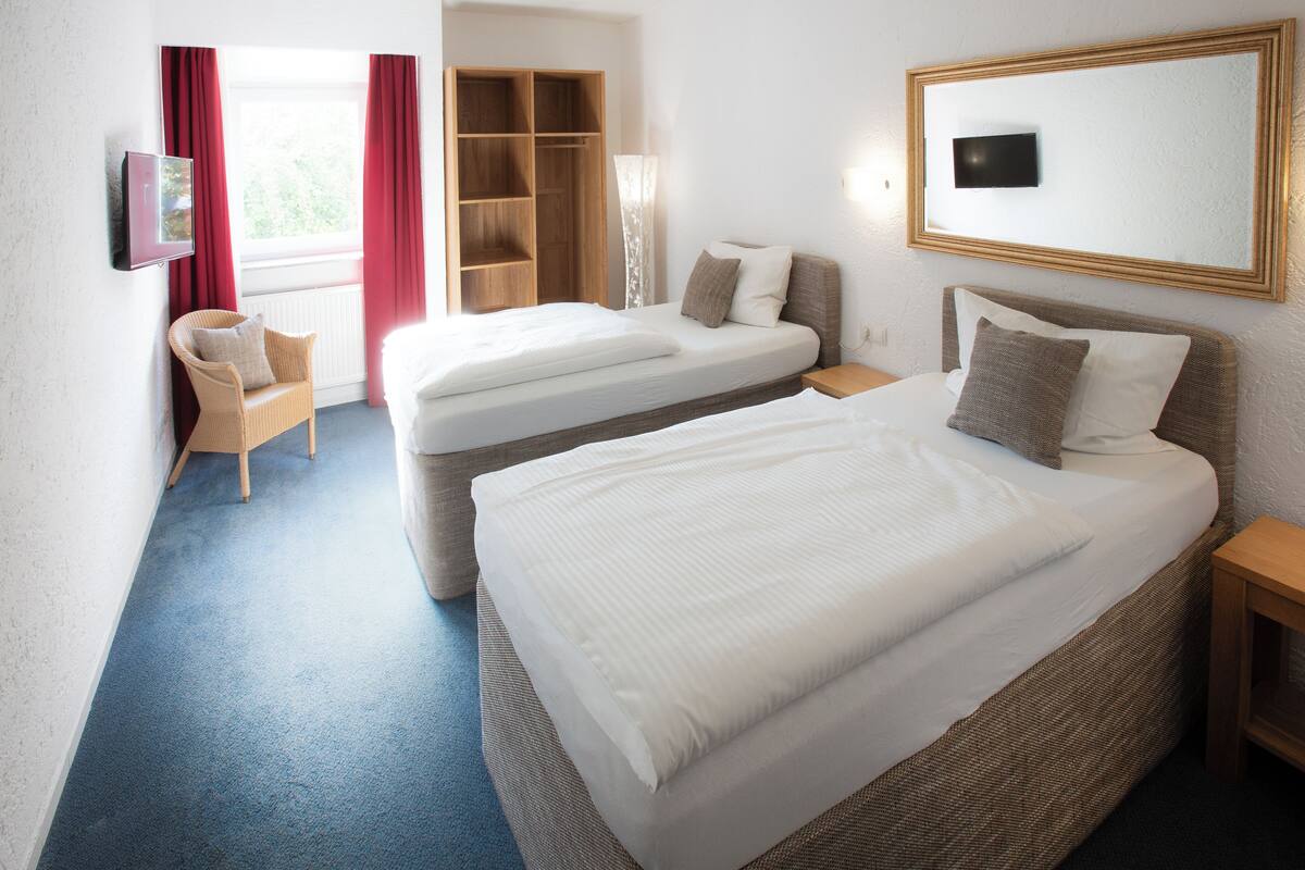 Ein Hotelzimmer mit zwei Betten, einem Schrank, einem Fernseher und einem Sessel.