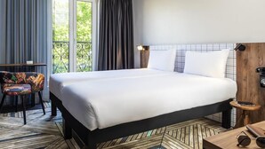 A hotel room with a bed, a chair, a small table, and a view of greenery outside. - ibis Styles Paris Gare de Lyon Bastille (Paris)