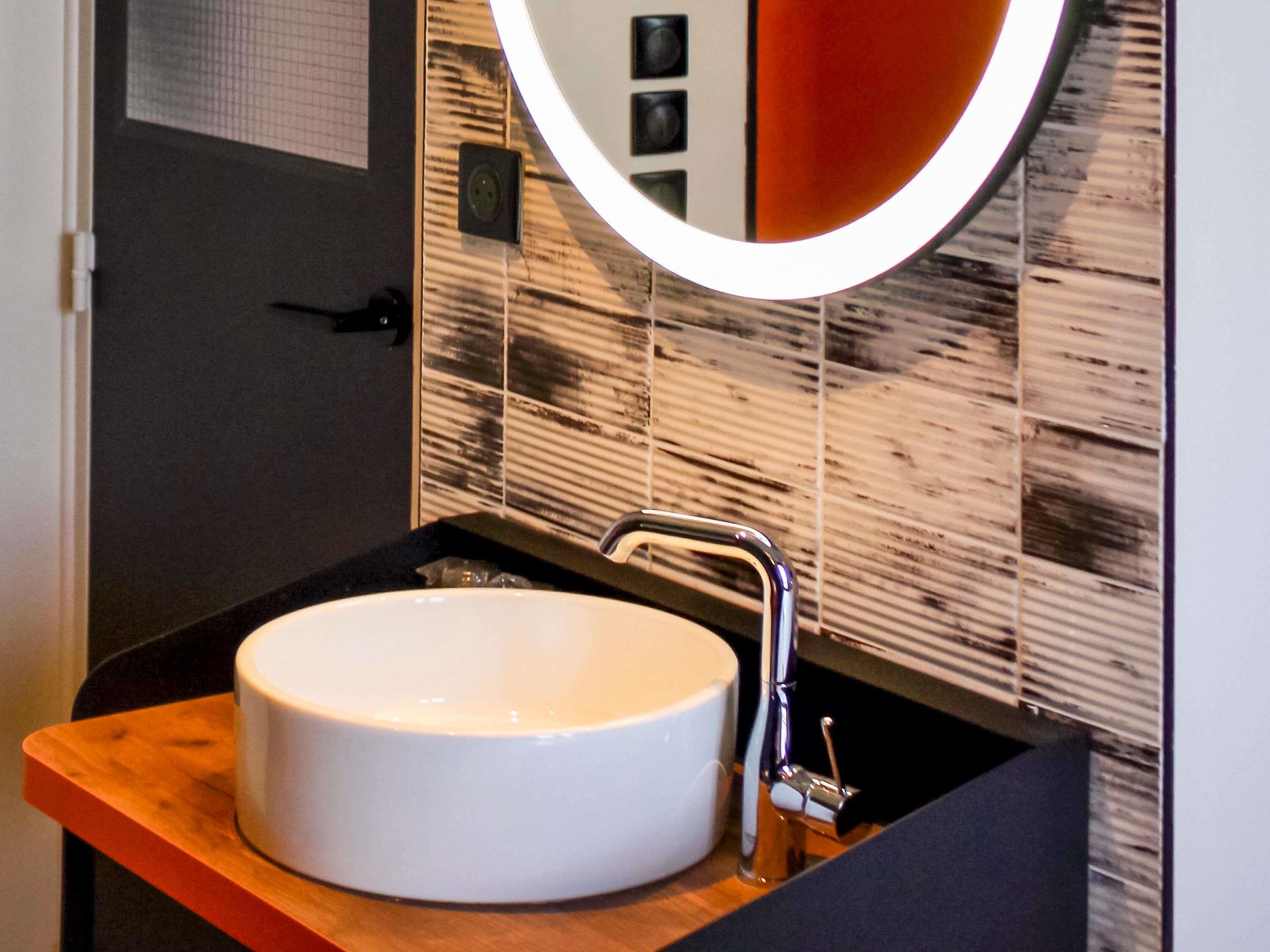 A bathroom with a white sink, a chrome faucet, and a mirror with a circular frame.