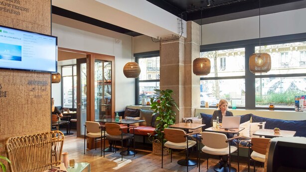 A modern cafe with wooden flooring, wicker chairs, and a large window offering a view of the street. - ibis Styles Paris Gare de Lyon Bastille (Paris)