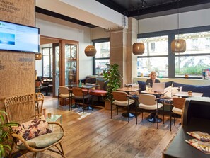 Un interior moderno con suelo de madera, diversas opciones de asientos incluyendo sillas y un sofá, y ventanas amplias que proporcionan luz natural.