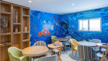 A children's playroom with a mural of underwater scenes, wooden shelves, and various seating arrangements.