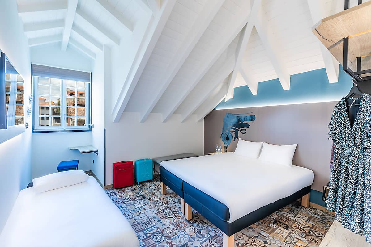 Un dormitorio con una cama grande, un banco, una ventana y un techo con vigas de madera.
