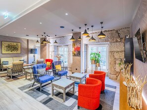 Un hall d’hôtel moderne offrant différents types de sièges, une cheminée et une grande fenêtre laissant entrer la lumière naturelle.