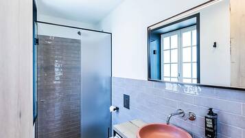 Un baño moderno con cabina de ducha de vidrio, un inodoro blanco, un lavabo rosa y un espejo con marco azul.