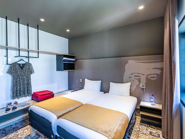 Habitación de hotel con una cama grande, una mesita de noche con una botella de agua, un perchero y un estante en la pared.