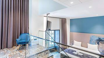 Una habitación de hotel moderna con una escalera de cristal, una cama, una silla azul y un suelo con estampado.