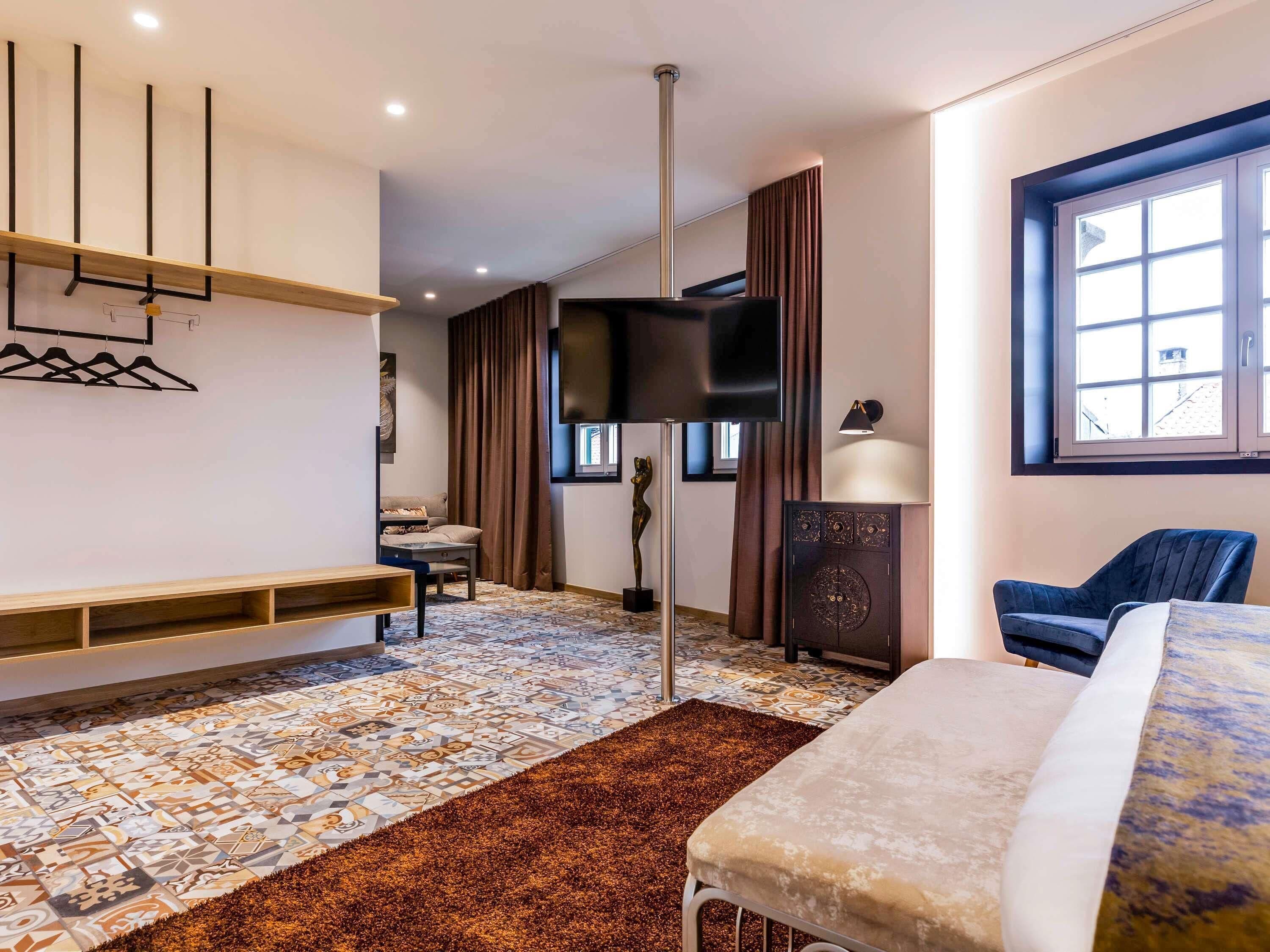 A modern hotel room with a bed, a TV, a desk, and a large window.