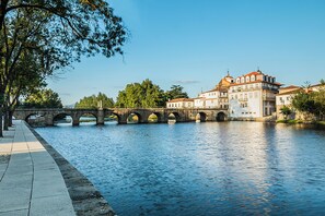 A stone bridge over a river with buildings on the opposite bank. - Ibis Styles Chaves  (Chaves)