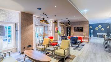 En modern hotellobby med en blandning av sittgrupper, en receptionsdisk och en stor TV-skärm.