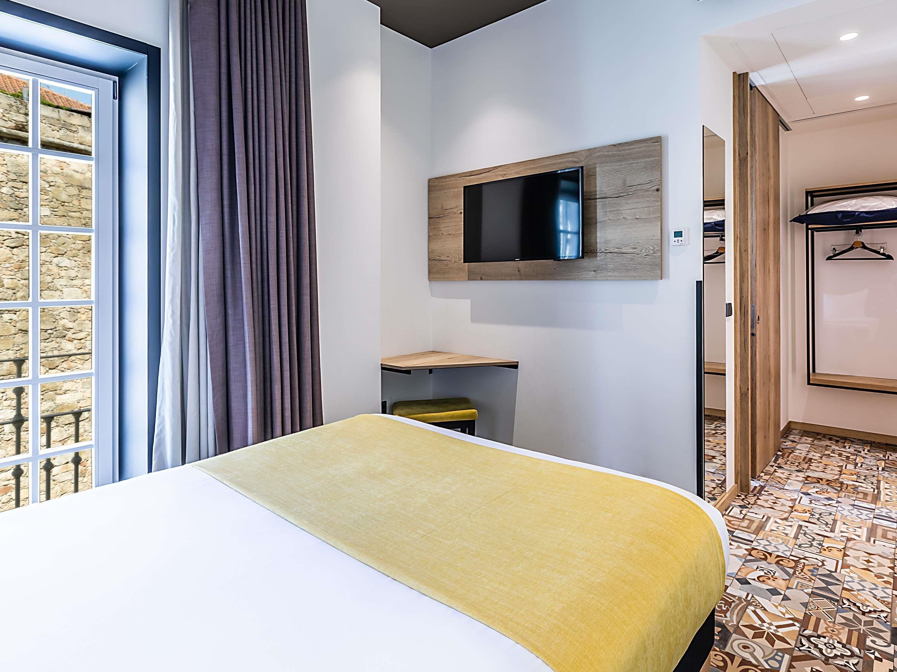 Habitación de hotel con cama, televisor montado, escritorio y baño con ducha.