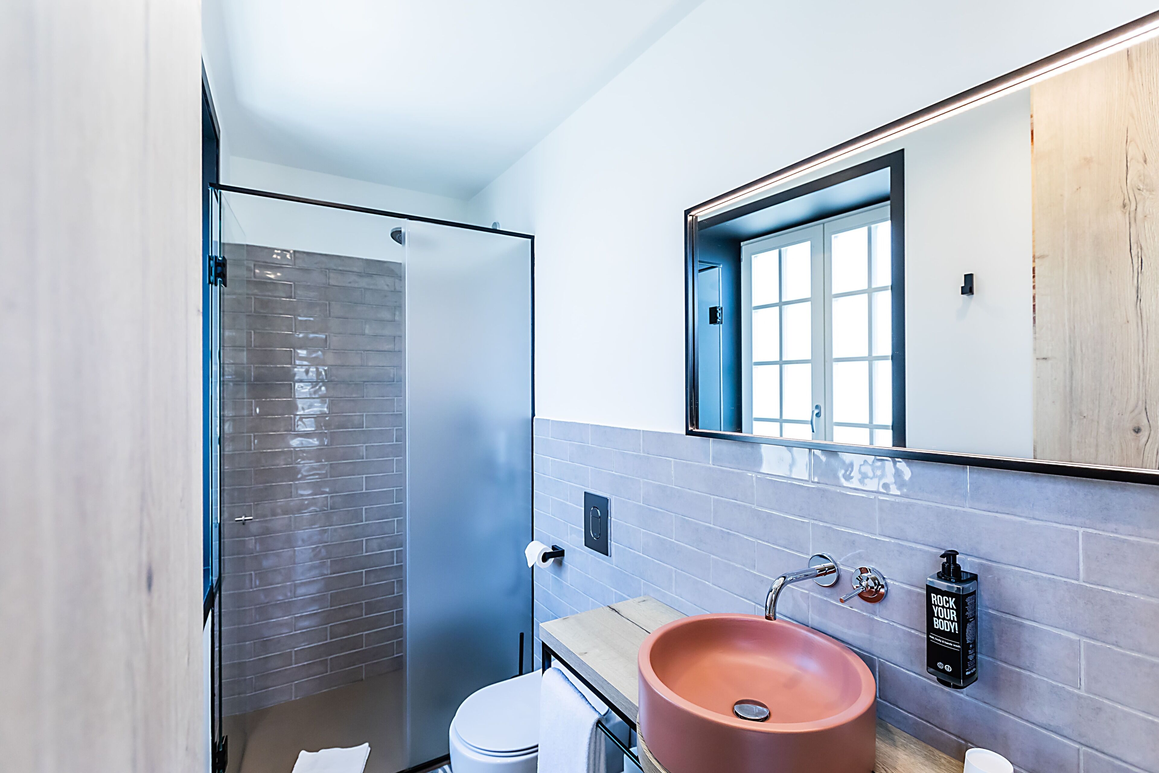 A modern bathroom with a glass shower enclosure, a wooden vanity, and a large mirror.