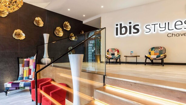 Moderni sisustus, jossa on portaikko, punaiset tuolit ja seinä, jossa on «ibis Styles» -kyltti.