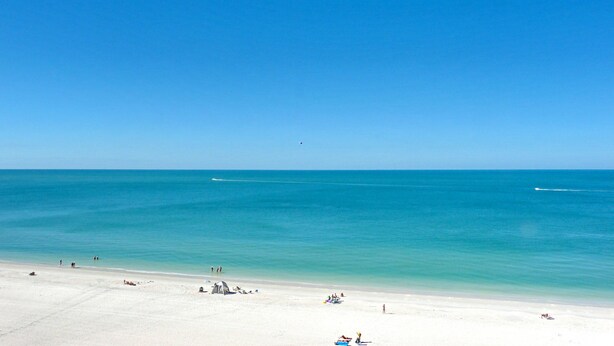 A beach with a clear sky, calm sea, and a few people and tents on the sand. - Beachfront Condo With Huge Views/pools/tennis/grills (Marco Island)