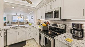 A modern kitchen with white cabinetry, a built-in microwave, a stove, and a coffee maker. - Beachfront Condo With Huge Views/pools/tennis/grills (Marco Island)