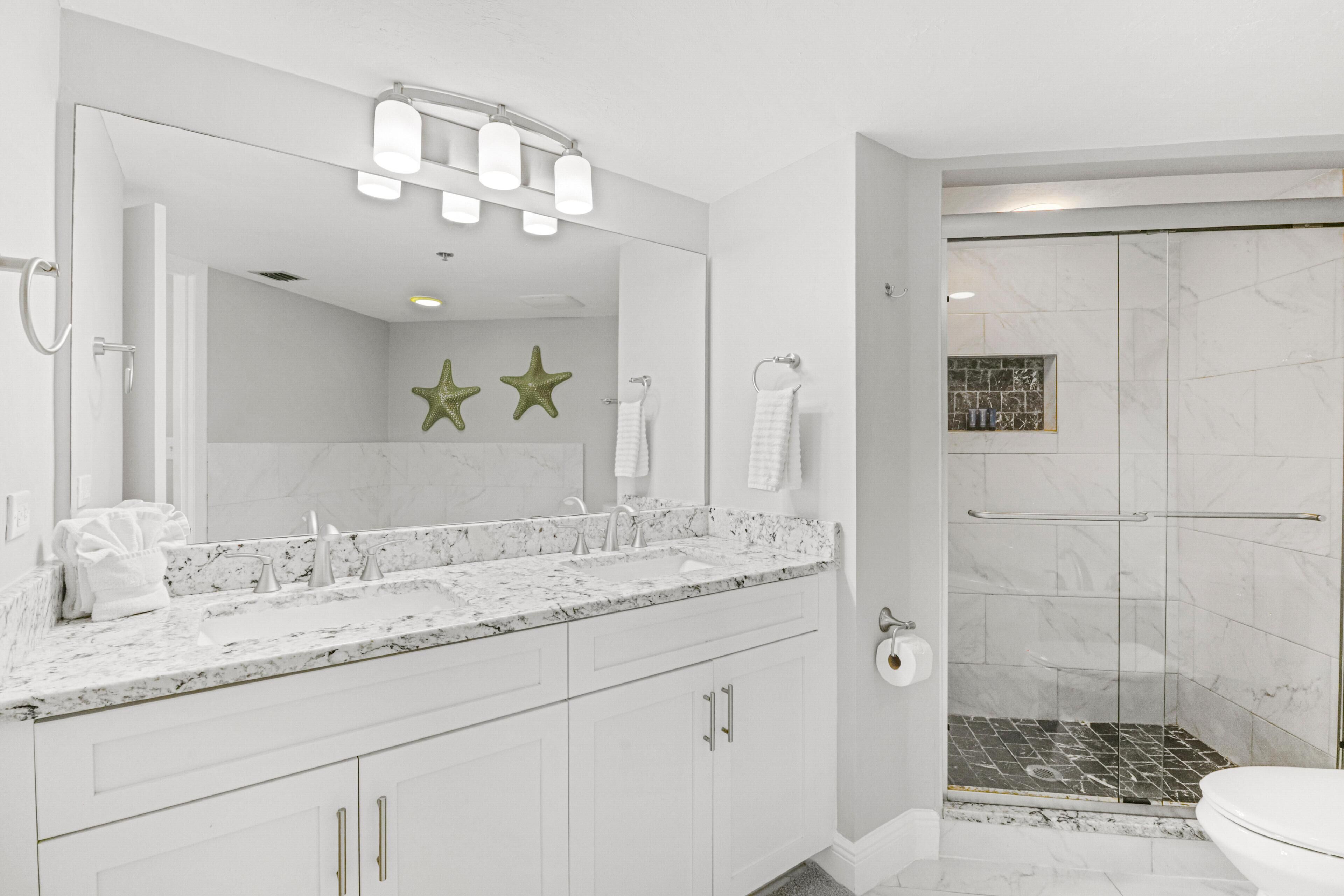 A modern bathroom with a large mirror, white vanity, and a shower area.